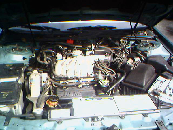 Engine bay of a light green Ford Taurus showing 3.0 V6 engine, air box, and battery