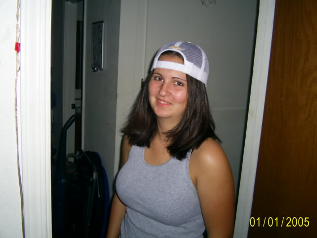 Young woman in gray tank top and backwards white mesh cap smiling in a doorway, 2005 date stamp