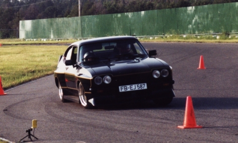 1981 Ford Mustang - A black coupe navigates a race track, marked by orange cones and a green fence in the background.