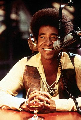 1991 Ford Bronco - Man with afro, headphones, and a patchwork vest smiles while sitting at a table with a drink.