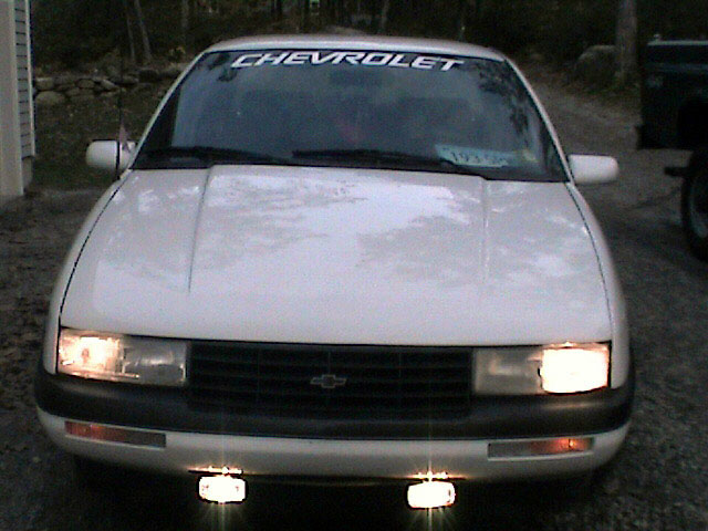 Front view of a white Chevrolet Corsica with a CHEVROLET windshield banner and lights on