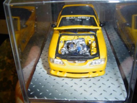 1979 Ford Bronco - Model car display a yellow Saleen with engine detail and a second car in the background.