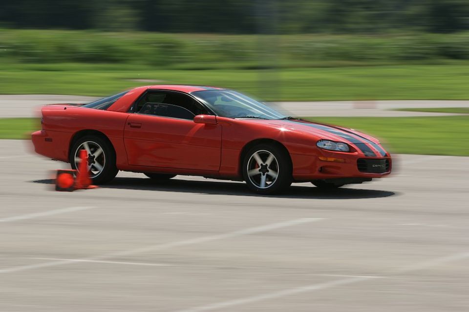 Red Chevrolet Camaro with black stripes cornering past traffic cones on an autocross course