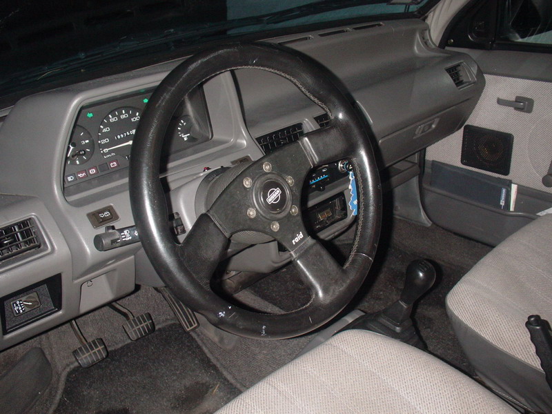 Gray car interior with aftermarket Raid three-spoke steering wheel, analog gauges and manual shifter