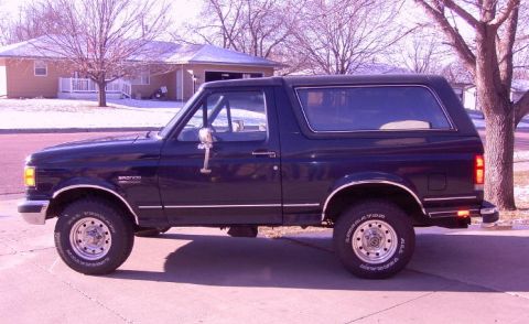 1990 Ford Bronco - A dark blue 1990 Ford Bronco is seen from the side, parked in front of a house with snow on the ground.