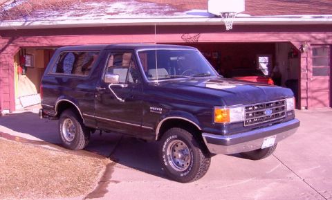 1990 Ford Bronco - Dark blue 1990 Ford Bronco parked in front of a garage with a basketball hoop overhead.