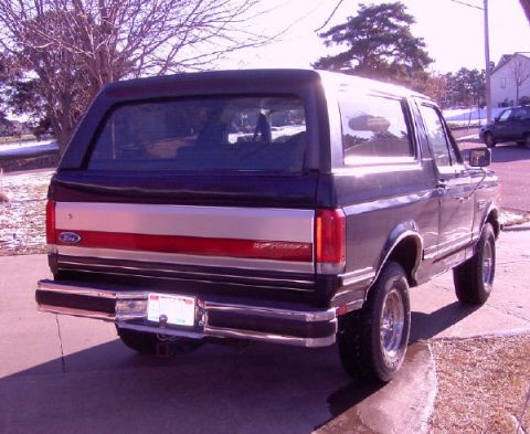 1990 Ford Bronco - The rear of a dark-colored Ford Bronco with a silver and red stripe on the tailgate is shown.