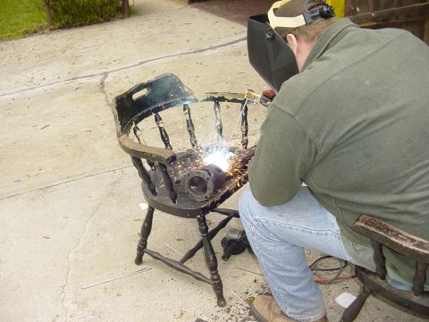 1989 Ford Bronco - A person welds metal components onto a wooden chair outdoors.