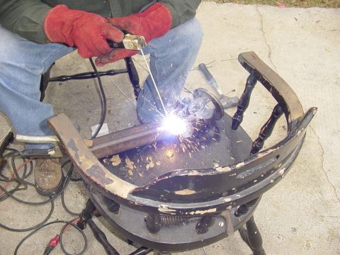 1989 Ford Bronco - A person in red gloves welds metal pieces onto a damaged wooden chair.