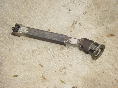 1989 Ford Bronco - A driveshaft with visible universal joints and a welded extension lies on the ground.