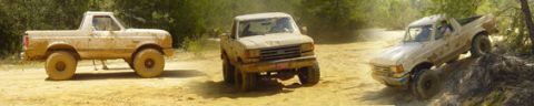 1996 Ford Bronco - Three trucks navigate a dusty, off-road trail, kicking up dirt as they go.