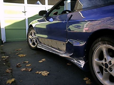 1993 Ford Probe - This vehicle shows extensive damage to its lower side panel and rocker area, indicating a significant impact.