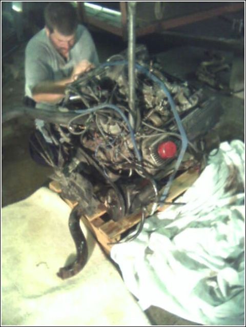 1980 Ford Bronco - Engine assembly being worked on by a person, resting on a wooden pallet.