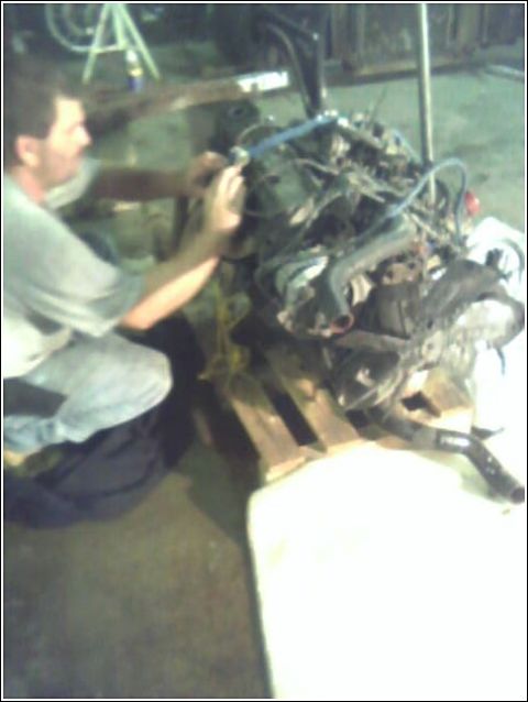 1980 Ford Bronco - A person is working on an engine assembly that is mounted on a wooden pallet.