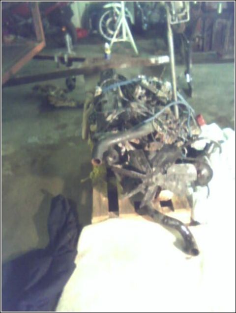 1980 Ford Bronco - Engine assembly with various hoses and wiring, resting on a wooden pallet in a workshop.
