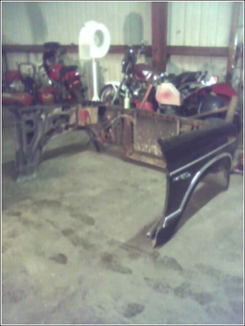 1980 Ford Bronco - A partial view of a vehicle chassis and fender is visible in a garage setting with motorcycles in the background.