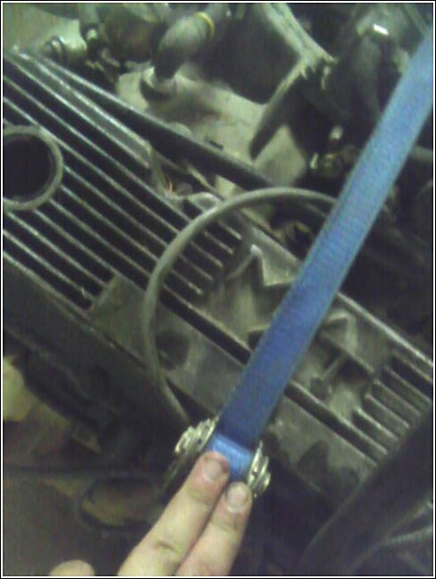 Engine block with blue strap and metal clamps being held by fingers