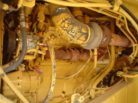 1966 International School Bus - Close-up view of a complex engine compartment, yellow piping and hoses, with a prominent exhaust system and turbocharger.