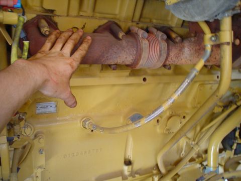 1966 International School Bus - Close-up of an engine's exhaust manifold and associated piping, with a hand present for scale.