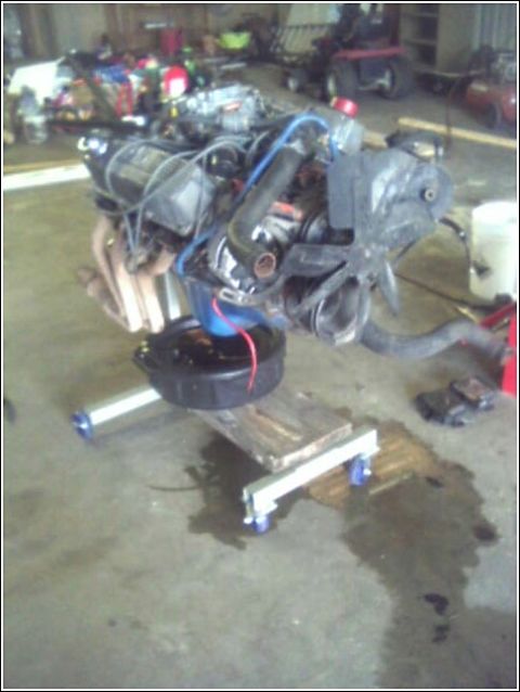 1980 Ford Bronco - Engine assembly is supported by a rolling stand in a garage setting.