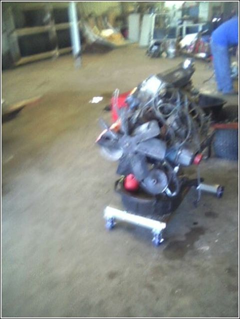 1980 Ford Bronco - An engine is displayed on a stand in a workshop, with a person visible in the background.