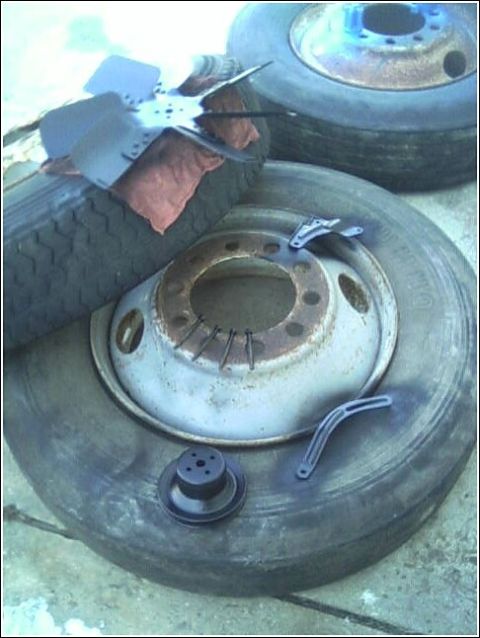 1980 Ford Bronco - Engine fan and other automotive parts are placed on tires, possibly for painting or storage.