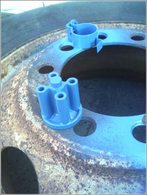 1980 Ford Bronco - A blue distributor cap and rotor sit on a heavily rusted wheel rim, suggesting a part replacement or repair.