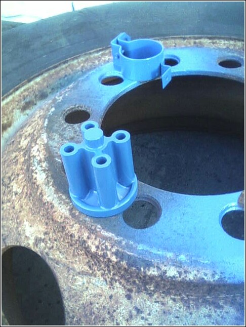 Blue plastic distributor cap and rotor on a rusty metal wheel rim with a tire edge visible