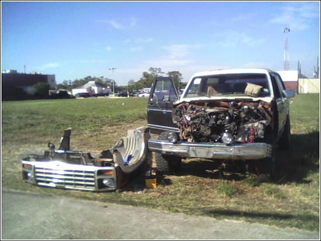 Truck with front end removed, engine exposed, sitting in a grassy field