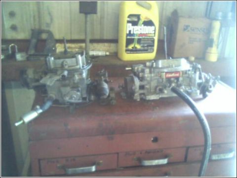 1980 Ford Bronco - Two carburetors are displayed on a workbench next to a bottle of Prestone coolant and a flashlight.