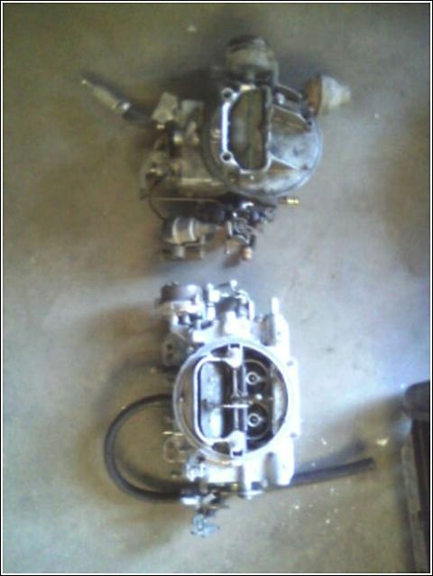 1980 Ford Bronco - Two carburetors are shown on a concrete surface, possibly for engine repair or replacement.