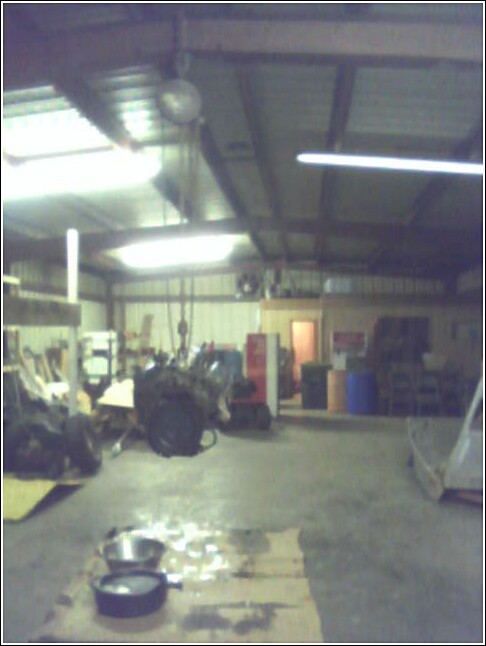 Engine hanging in a workshop, with tools and barrels in the background
