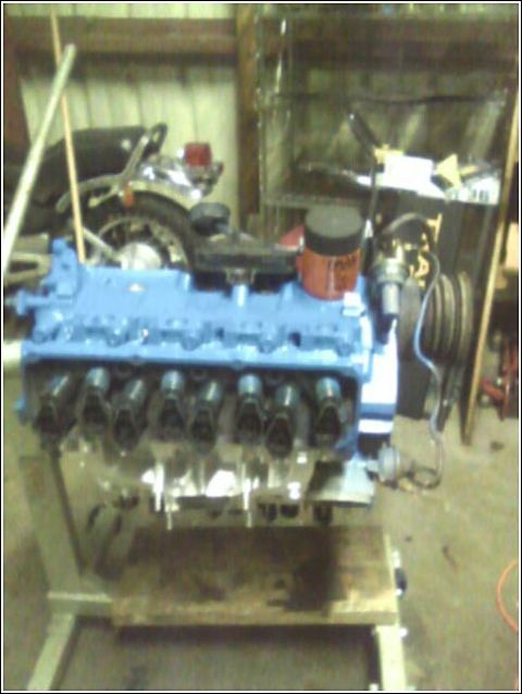 1980 Ford Bronco - A V8 engine is displayed on a stand, with a motorcycle partially visible behind it.
