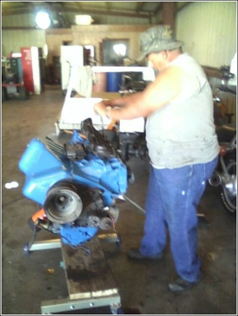 1980 Ford Bronco - A person is working on a blue engine that is mounted on a stand in a workshop.