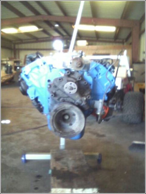 1980 Ford Bronco - A blue engine block is suspended by a hoist in what appears to be a workshop or garage setting.