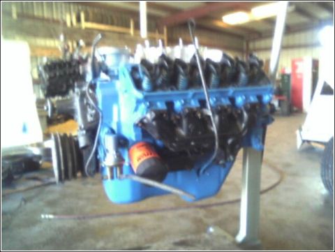 1980 Ford Bronco - A blue V8 engine is mounted on a stand in a workshop, with an orange oil filter attached.