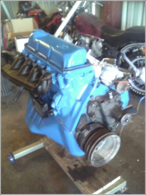 1980 Ford Bronco - A bright blue engine is mounted on a stand, with motorcycles visible in the background.