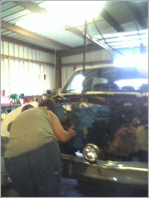 1980 Ford Bronco - An engine is being installed into a vehicle with the help of a chain hoist in a workshop.
