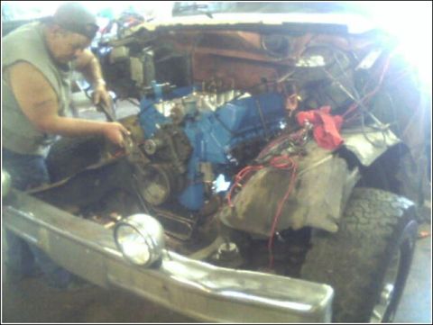1980 Ford Bronco - A mechanic works on the engine of a vehicle, with various parts and wiring exposed.