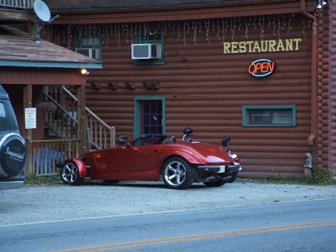1966 Ford Ranchero - A red convertible sports car is parked outside a log building with a neon open sign.