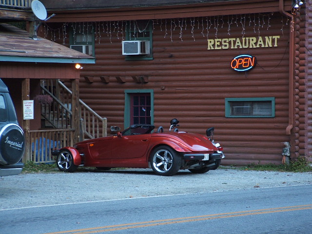 Red convertible sports car parked in front of a log building with a restaurant sign