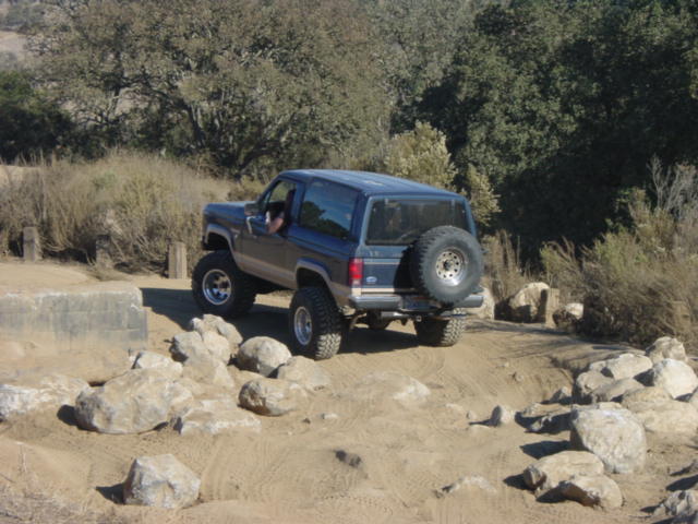 Blue SUV with spare tire on rear, driving over rocks on a dirt path