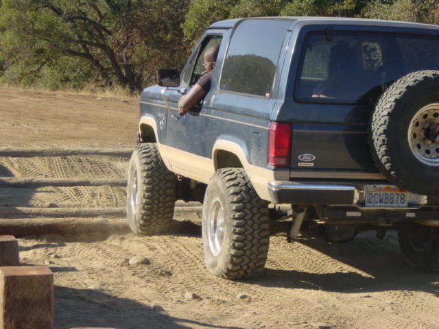 Dark blue and tan Ford Bronco II with off-road tires driving on a dirt path
