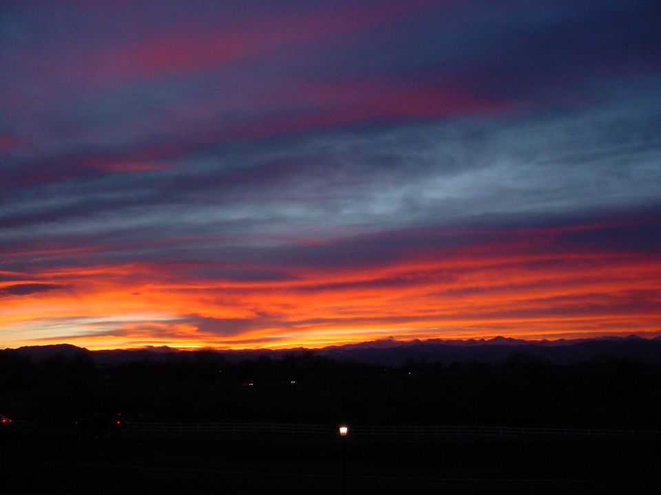 Sunset sky with vibrant orange, red, and purple clouds over a dark, silhouetted mountain range and landscape