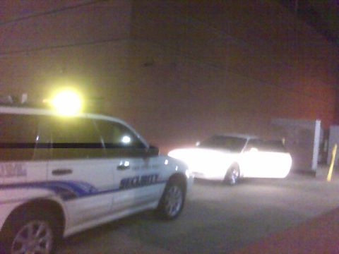 1996 Ford Probe - A security van with a light on top is parked next to a white car.