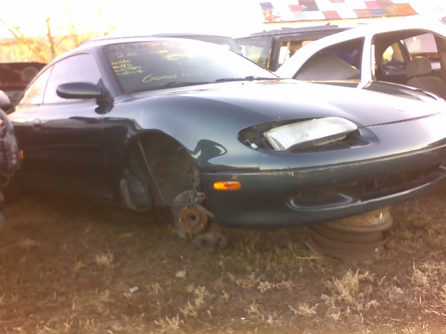 Dark green coupe with missing front wheels, headlights damaged, sitting on tires