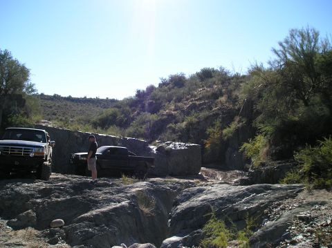 1993 Ford Bronco - A dark blue Ford F-Series truck is parked on a rocky trail, with another truck visible behind it.