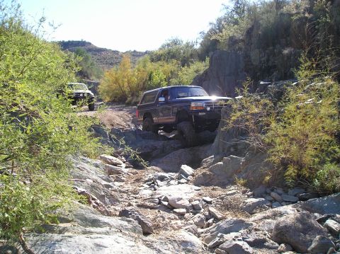 1993 Ford Bronco - Two SUVs tackle a challenging rocky path in a desert landscape.