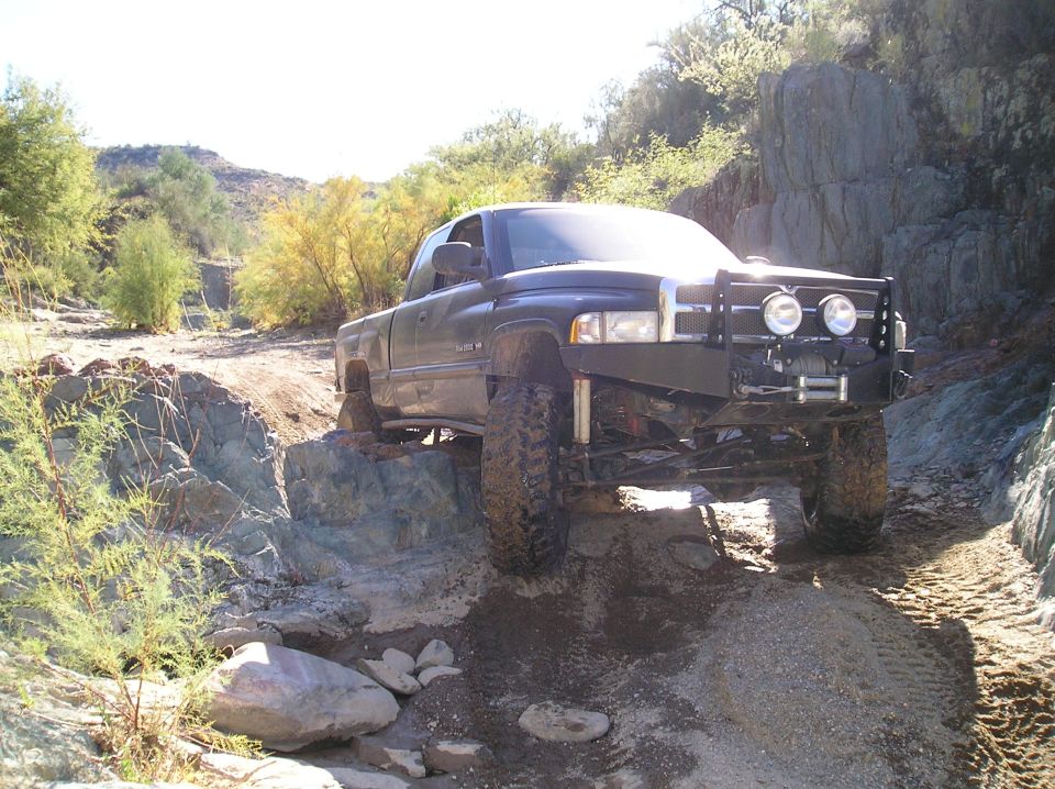Dark pickup truck with aftermarket bumper and winch navigating rocky terrain