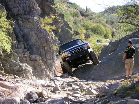 1993 Ford Bronco - A black 1993 Ford Bronco tackles a challenging rocky terrain, demonstrating its off-road capabilities while another vehicle follows behind.